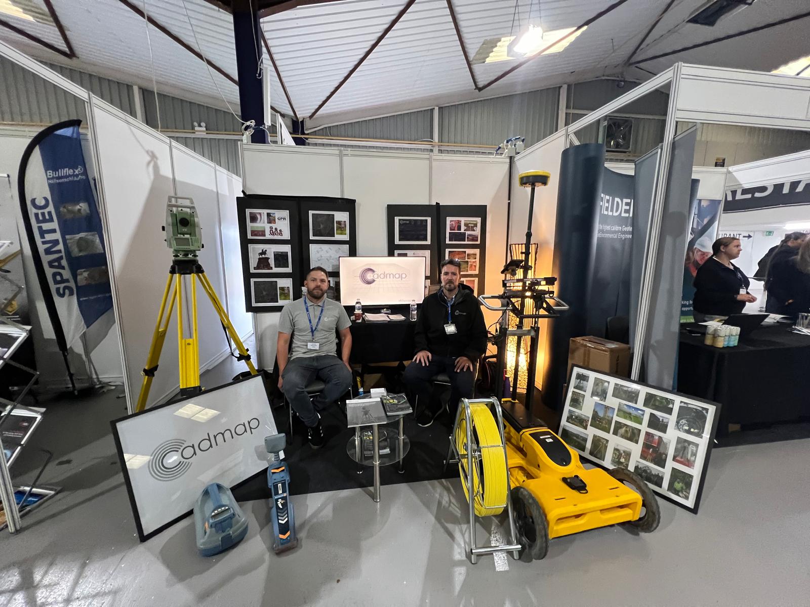 Two CADMAP representatives at an exhibition stand with surveying equipment