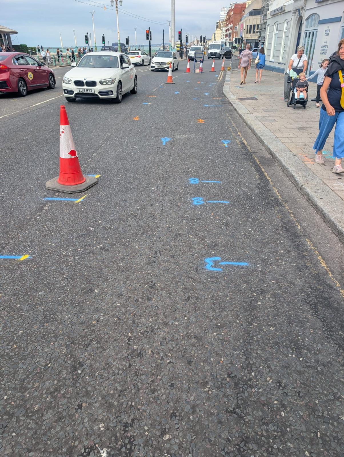 Roadside utility markings beside traffic cones, cars and pedestrians