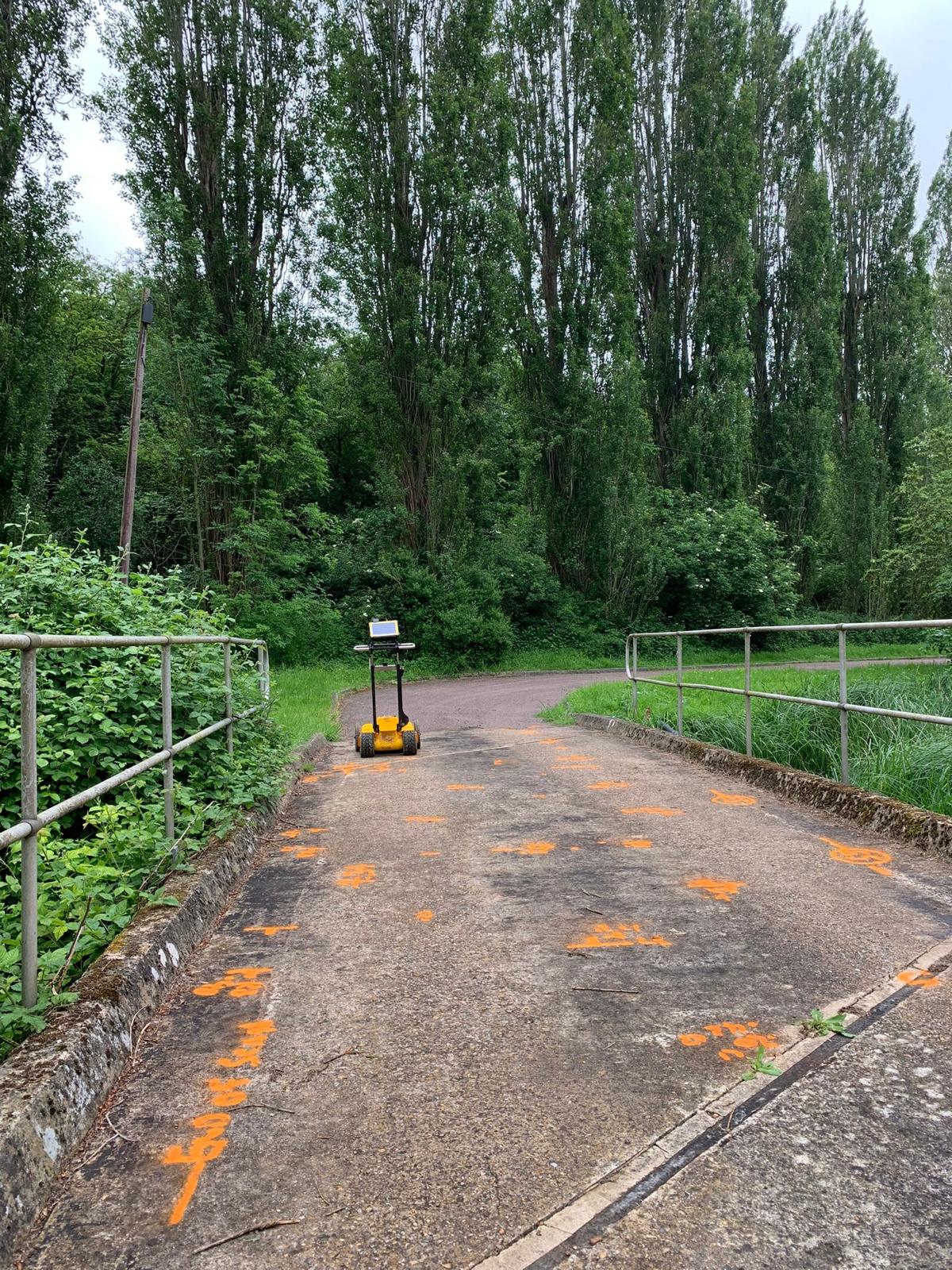 Yellow ground penetrating radar cart on a bridge beside orange utility markings