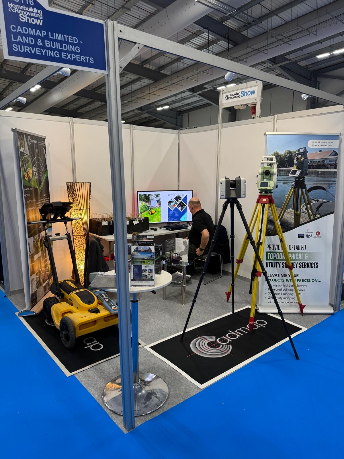 CADMAP exhibition stand with a man beside a display screen, surveying instruments and a radar cart